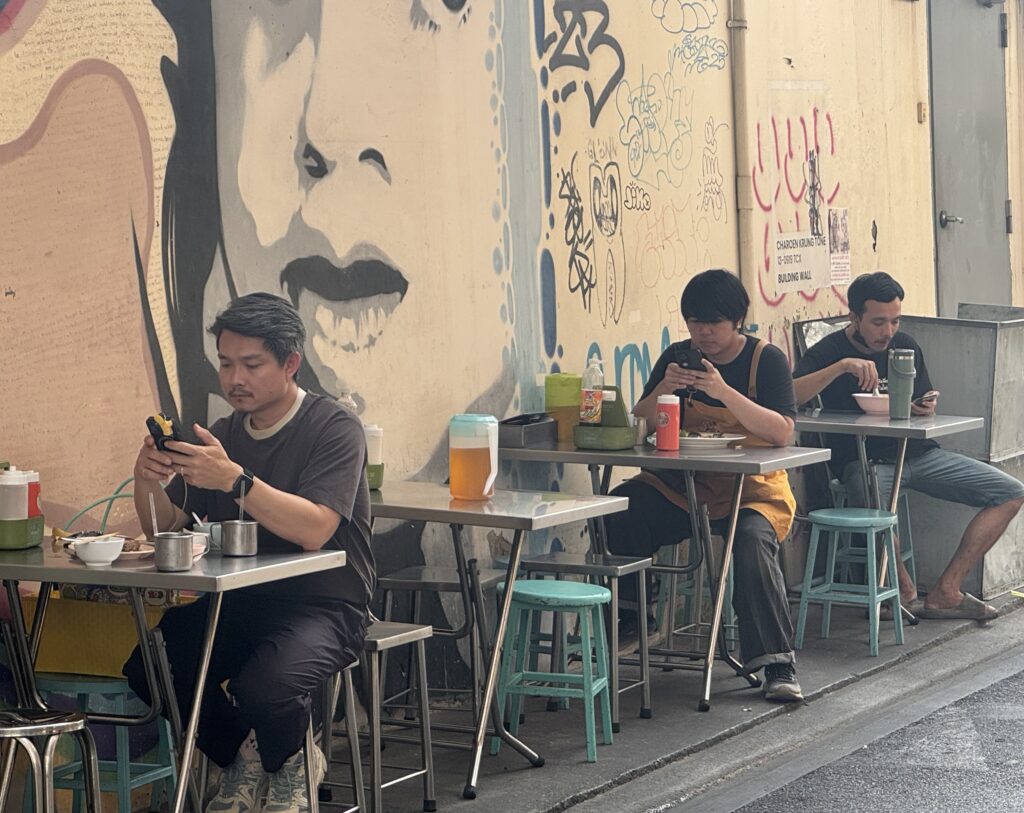 Trois jeunes hommes déjeunent à Talat Noi, l’inséparable portable en main. ©Corine Moriou